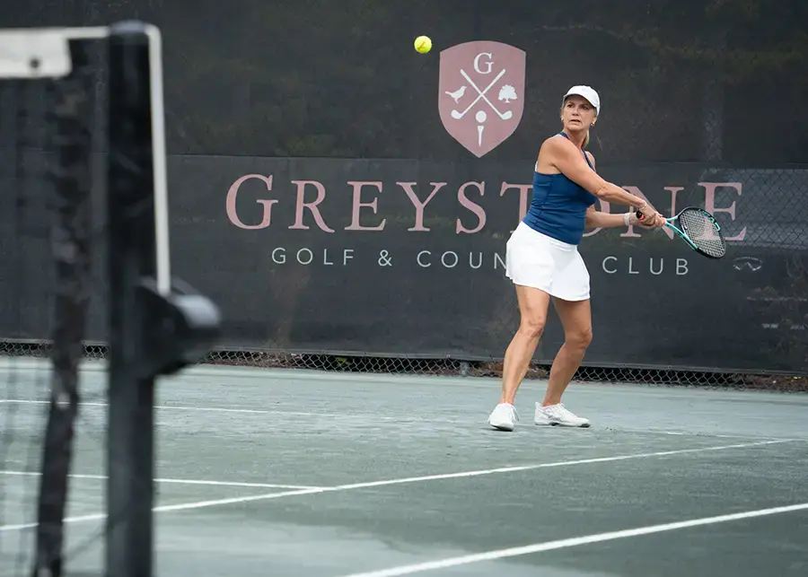 woman playing tennis greystone logo behind